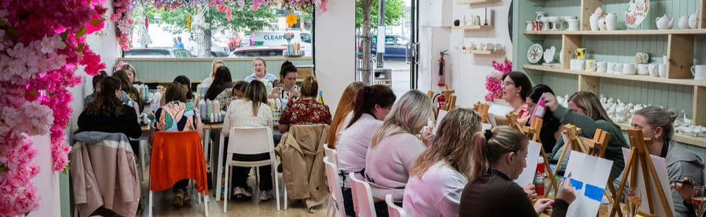 Interior ofstudio with pink floral decorations and people sitting at tables painting. 